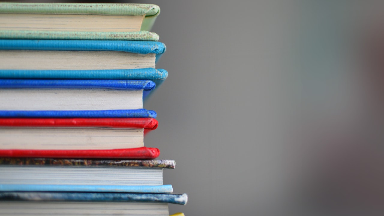 A stack of well-worn hardcover books on a wooden surface